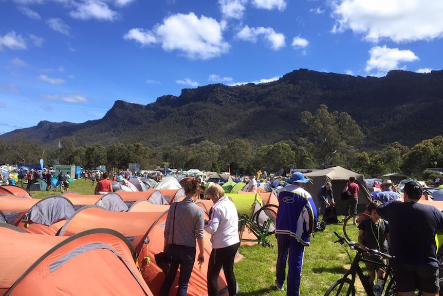 Many people camping with the Grampians mountains behind 