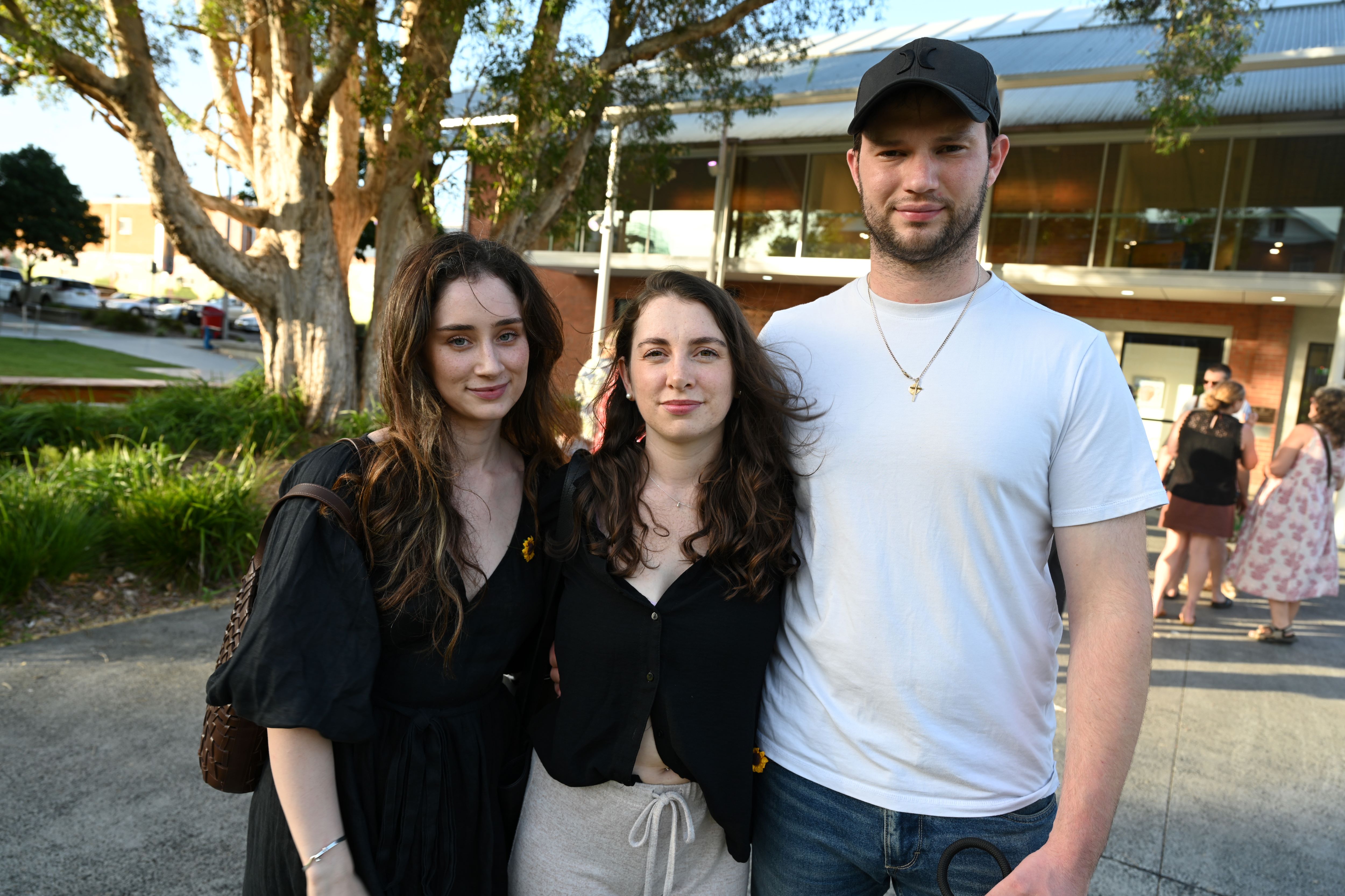 Two women and a man stand together closely and look at a camera