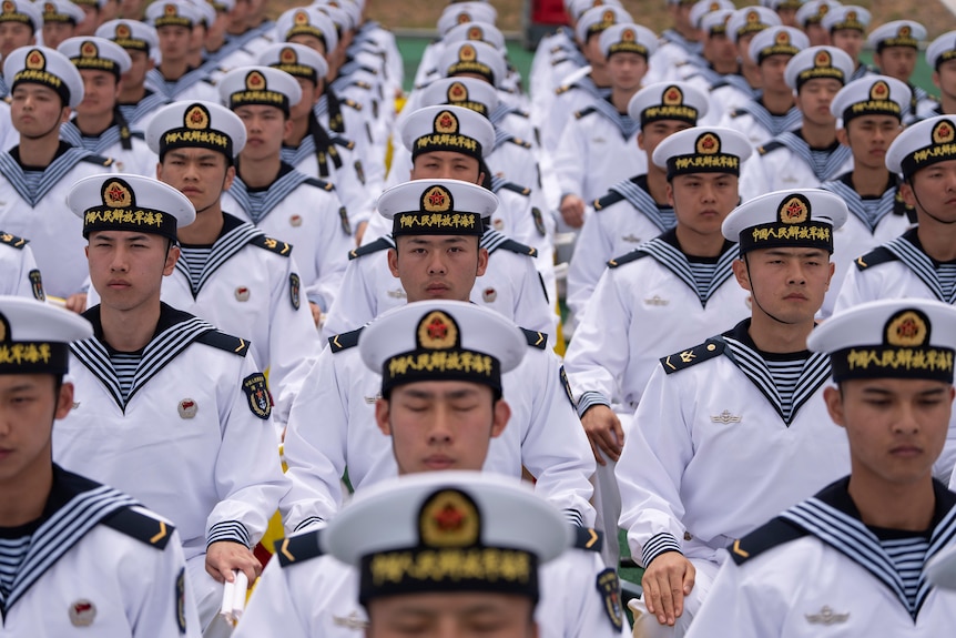 Uniformed Chinese sailors sit in rows,looking forwards with neutral expressions on many faces.