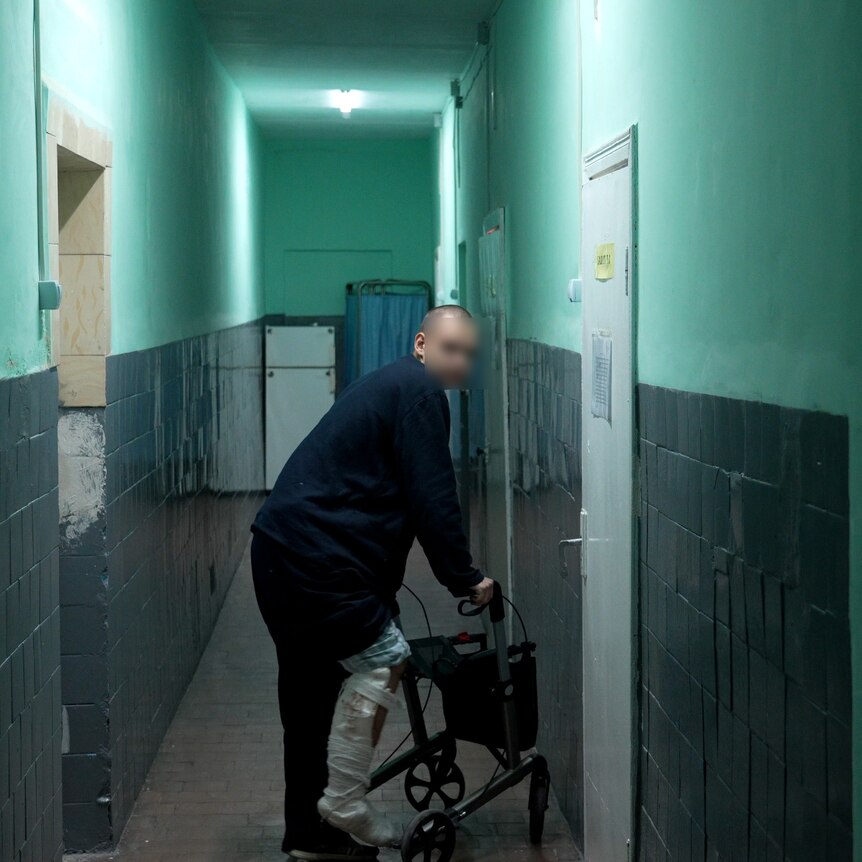 A young man using a walker stands in a lonely corridor.