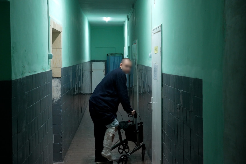 A young man using a walker stands in a lonely corridor.