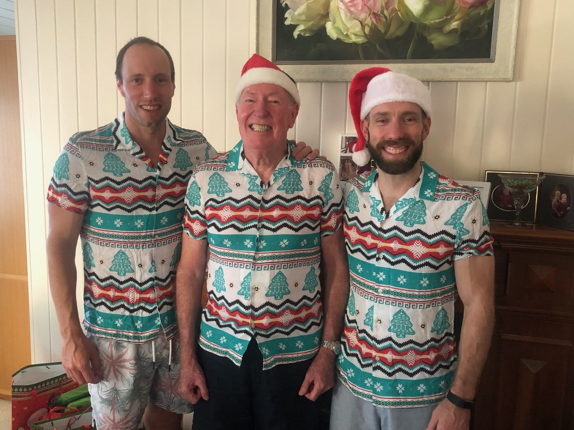 Three men stands side by side in matching Christmas outfits.