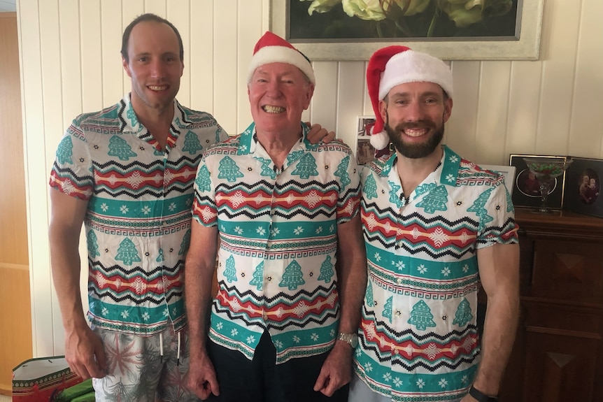 Three men stands side by side in matching Christmas outfits.