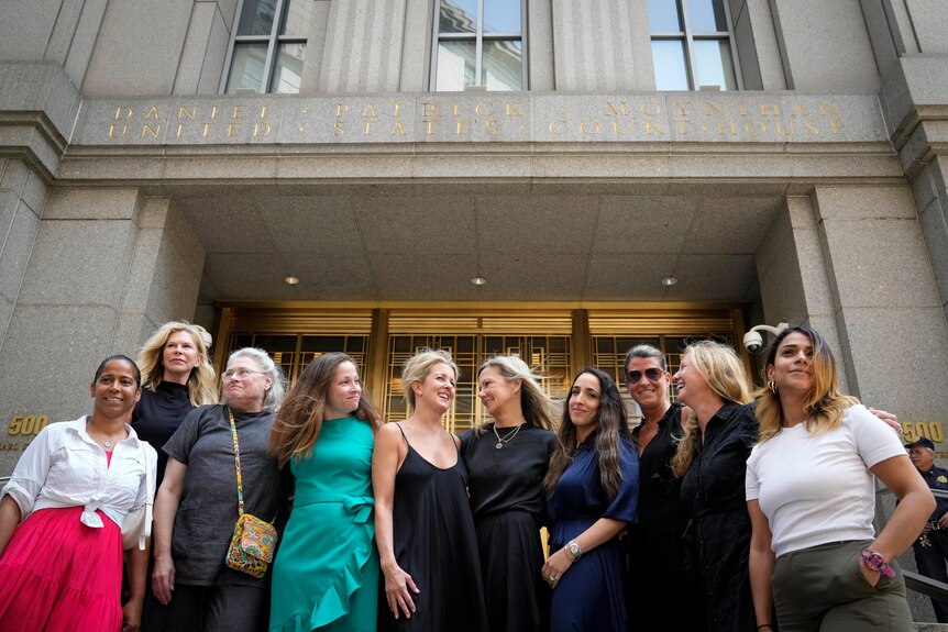 Ten women of varying ages and walks of life gather together and smile out the front of a courthouse