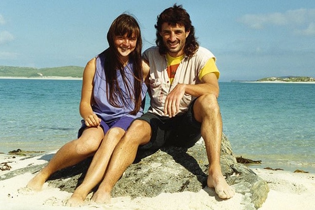 An old photo of a smiling young woman sitting with a young man on a rock on a beach
