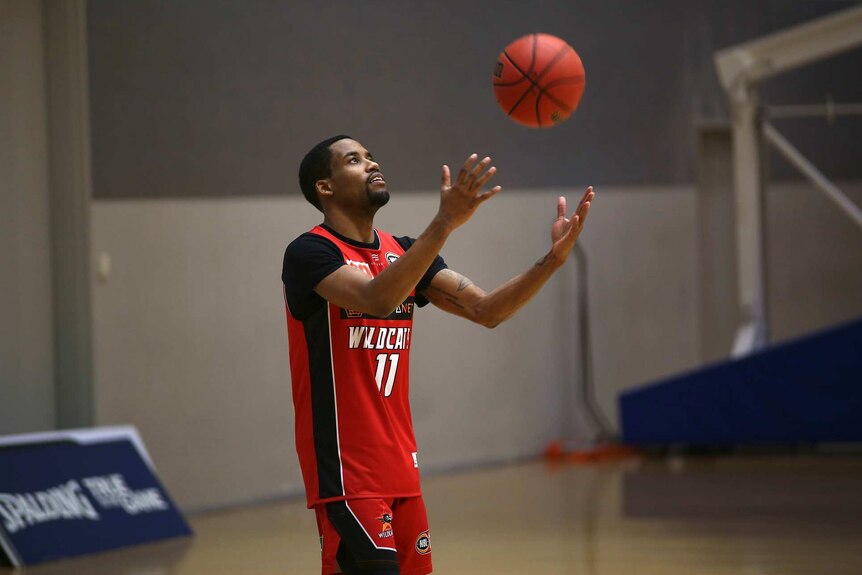 Perth Wildcats guard Bryce Cotton holds his arms out to catch a basketball during a training session in a gym.