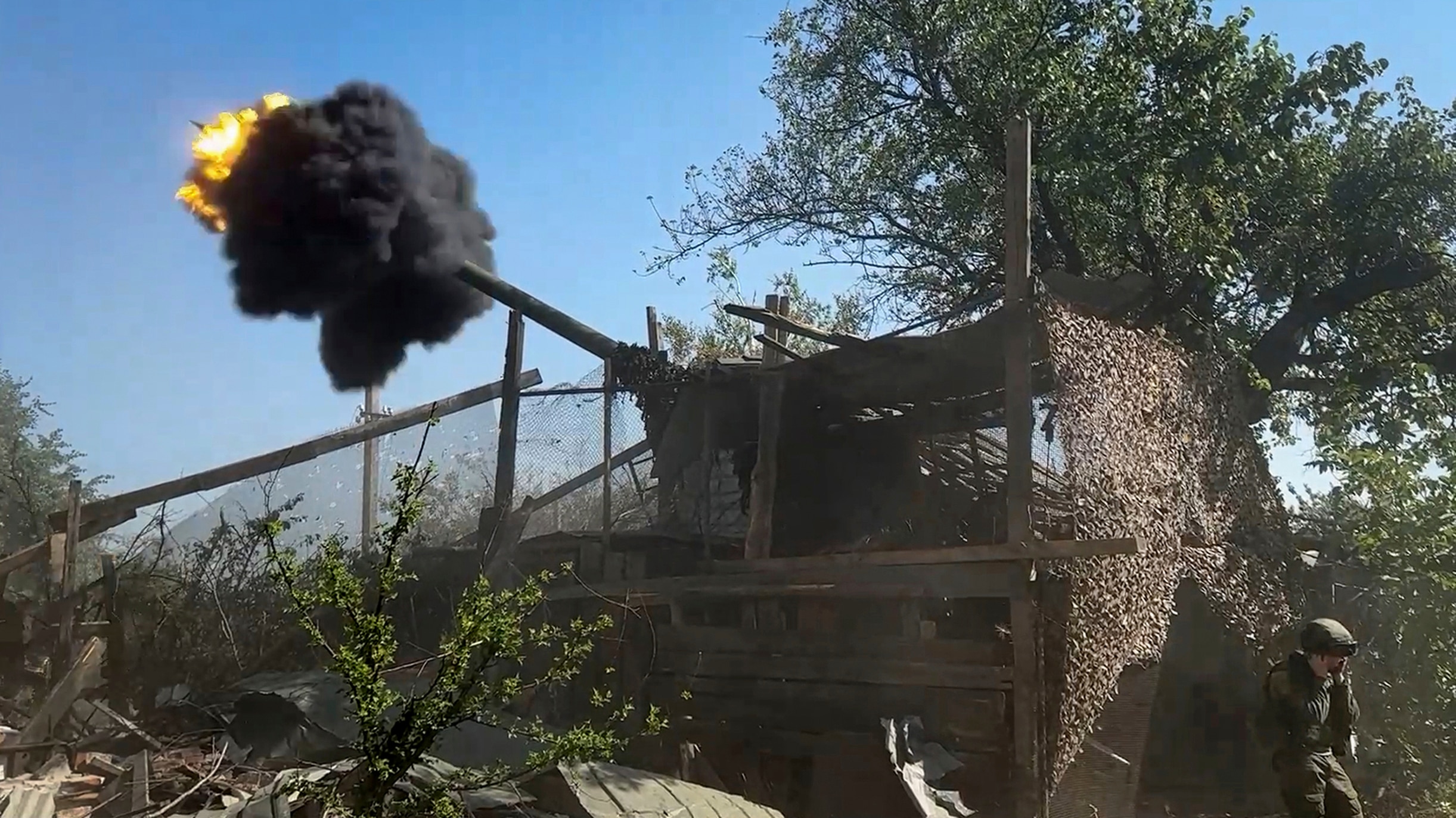 A small explosion erupts from a metal nozzle attached to a camouflaged structure.