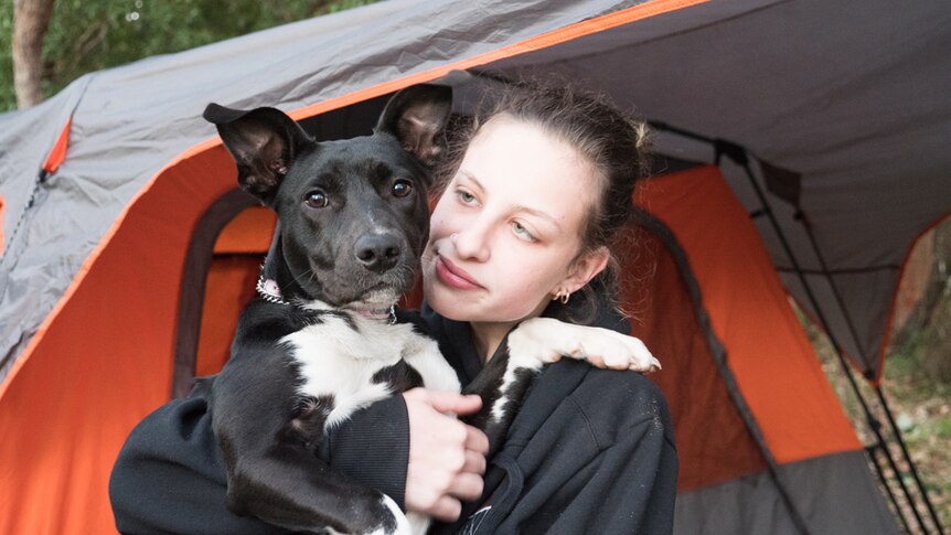 Teenage girl standing outside a tent holding a puppy