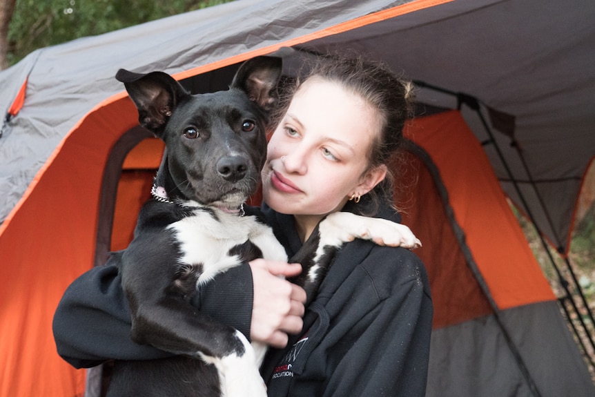 Teenage girl standing outside a tent holding a puppy