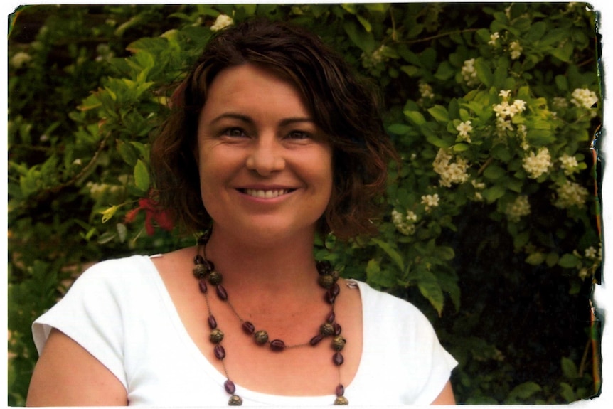 Kim Sinclair smiles while standing in front of some flowering plants.