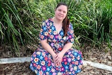Nataasha Torzsa smiles while sitting in front of garden. She's wearing a colourful floral dress.