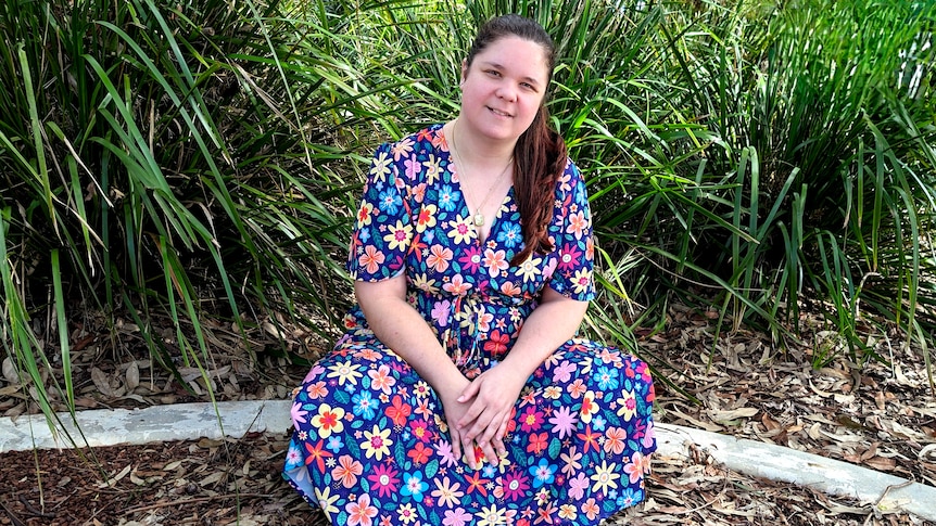 Nataasha Torzsa smiles while sitting in front of garden. She's wearing a colourful floral dress.