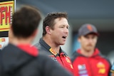 A man wearing a Gold Coast Suns jacket talks to a group of players.