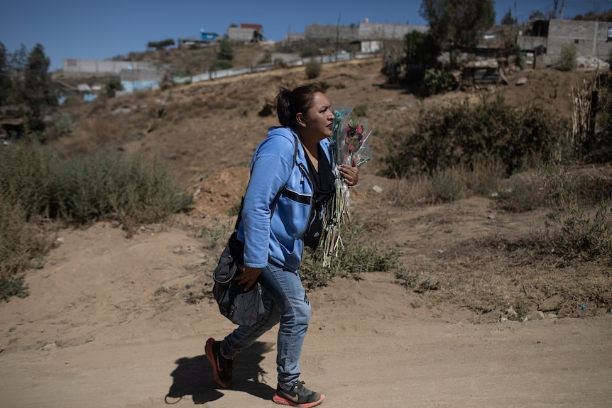 Angeles walks uphill holding flowers.