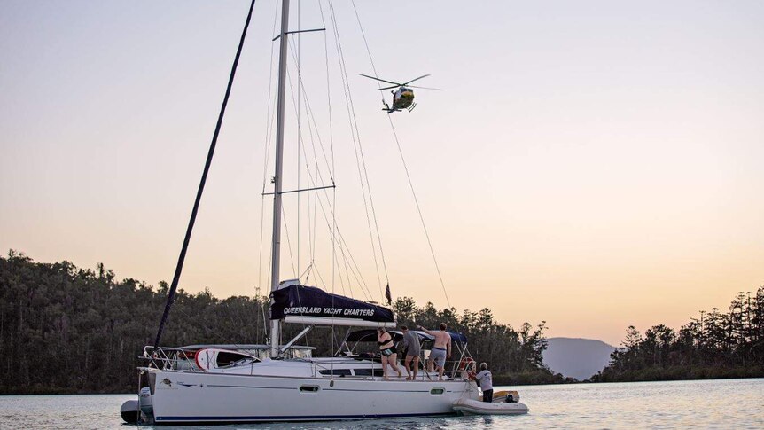 A helicopter hovers over a yacht at dusk