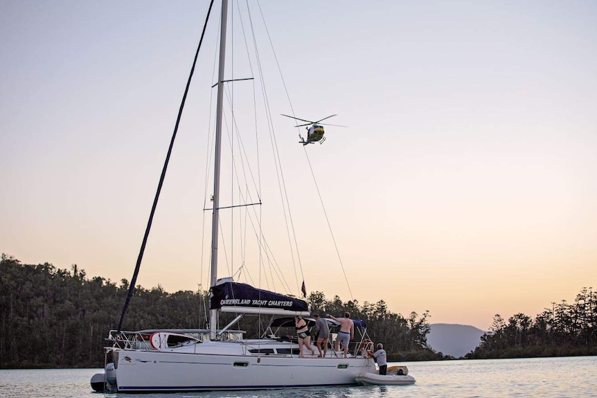 A helicopter hovers over a yacht at dusk