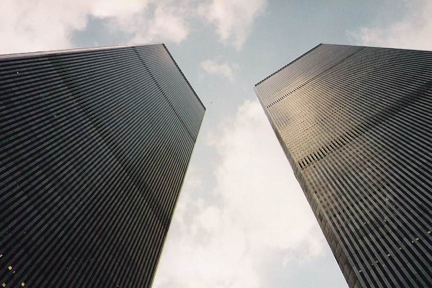 The Twin Towers (before 2001), shot from below, stretching towards a cloudy blue sky 