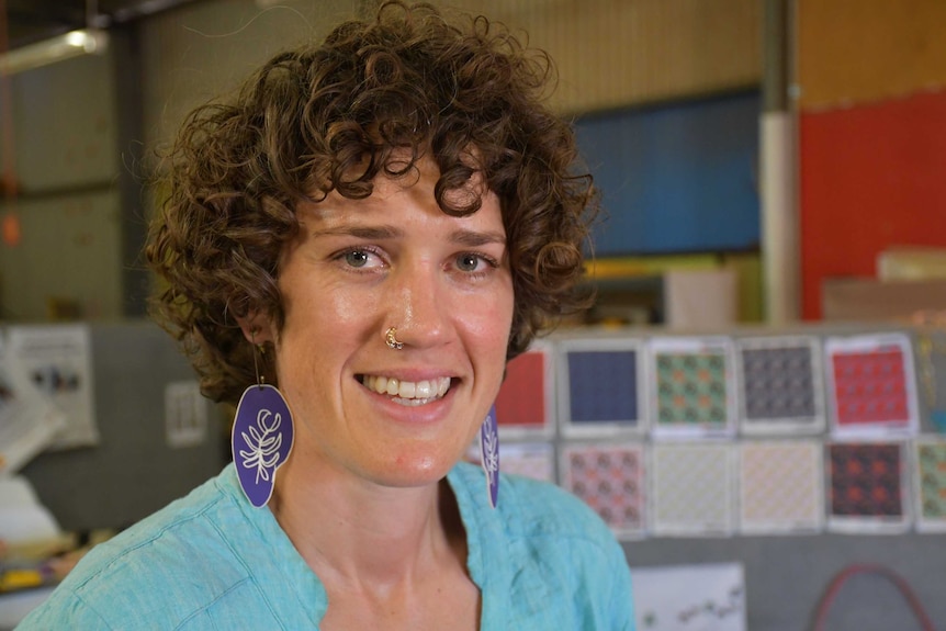 A lady with large ear rings and a nose rings smiles at the camera.