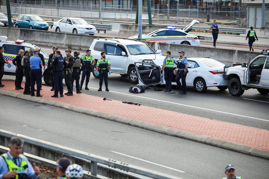 A man lies handcuffed on a road surrounded by police. 