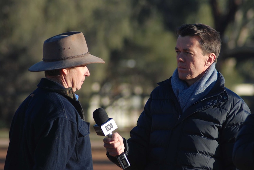 Rowland holding microphone interviewing farmer in a hat.