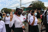 Women wearing white and holding up three fingers march down a road.