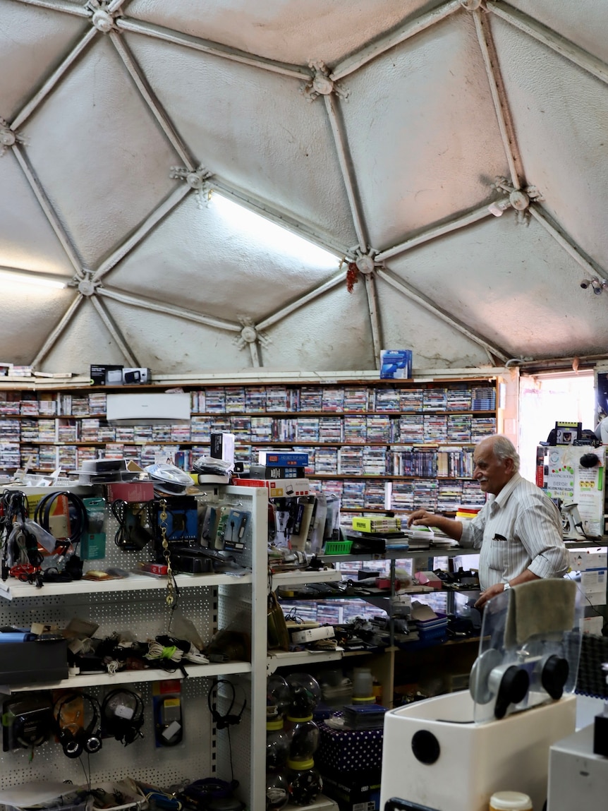 an old man behind the counter surrounded by shelvs full of DVDs 