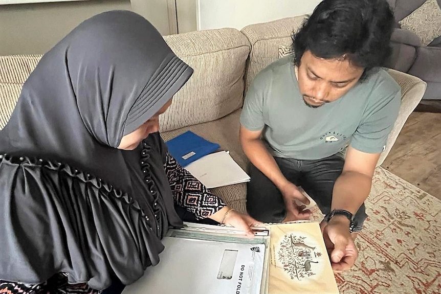 A woman in a headscarf and a man in a green T-shirt sitting on a couch looking through important documents.