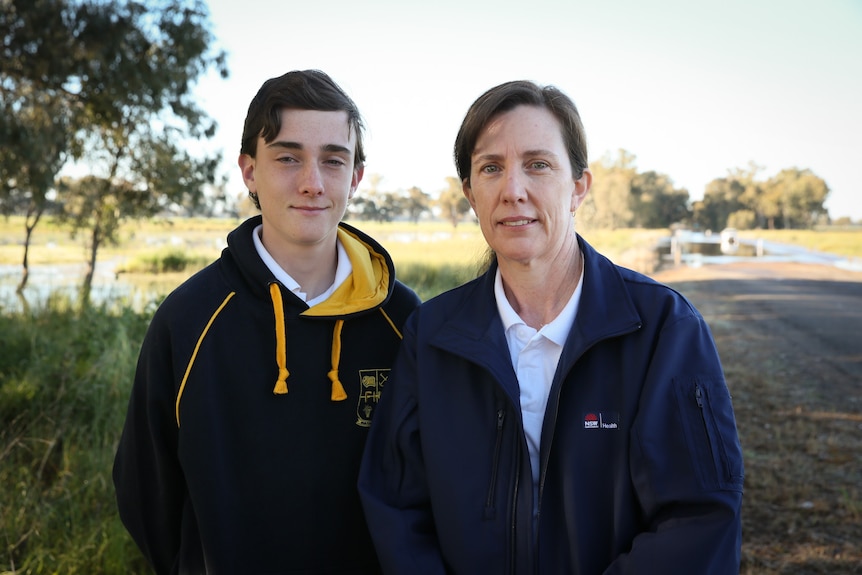 A teenage boy and a woman, both with dark hair, standing outside.