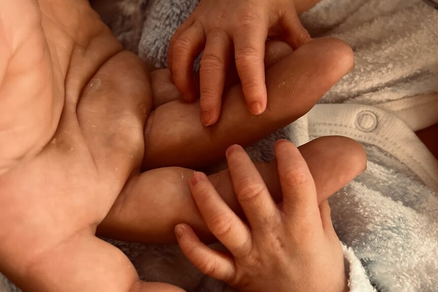 A close-up of a newborn baby's hands wrapped around a father's fingers.