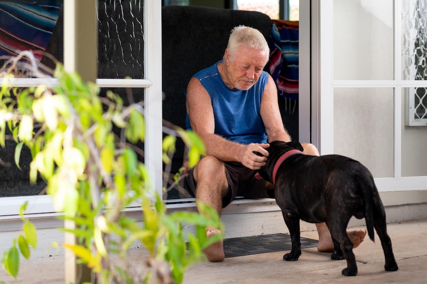 Man sits on back door step tickling black dog behind ears.