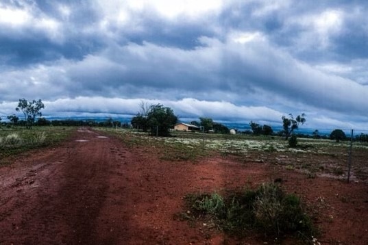 Overcast, rainy skies over red dirt and a house in the distance.
