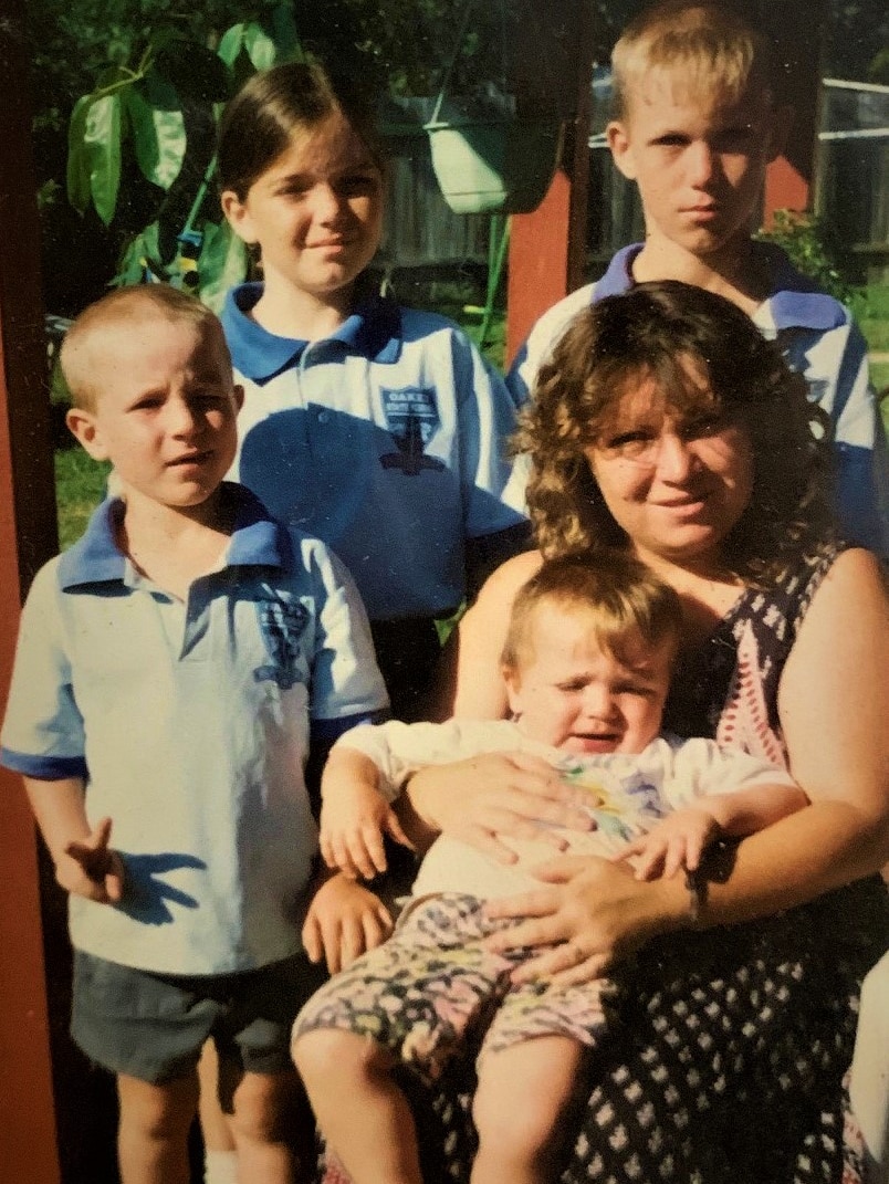 Four kids and their mum in a backyard home family photo. Three older kids in school uniform.