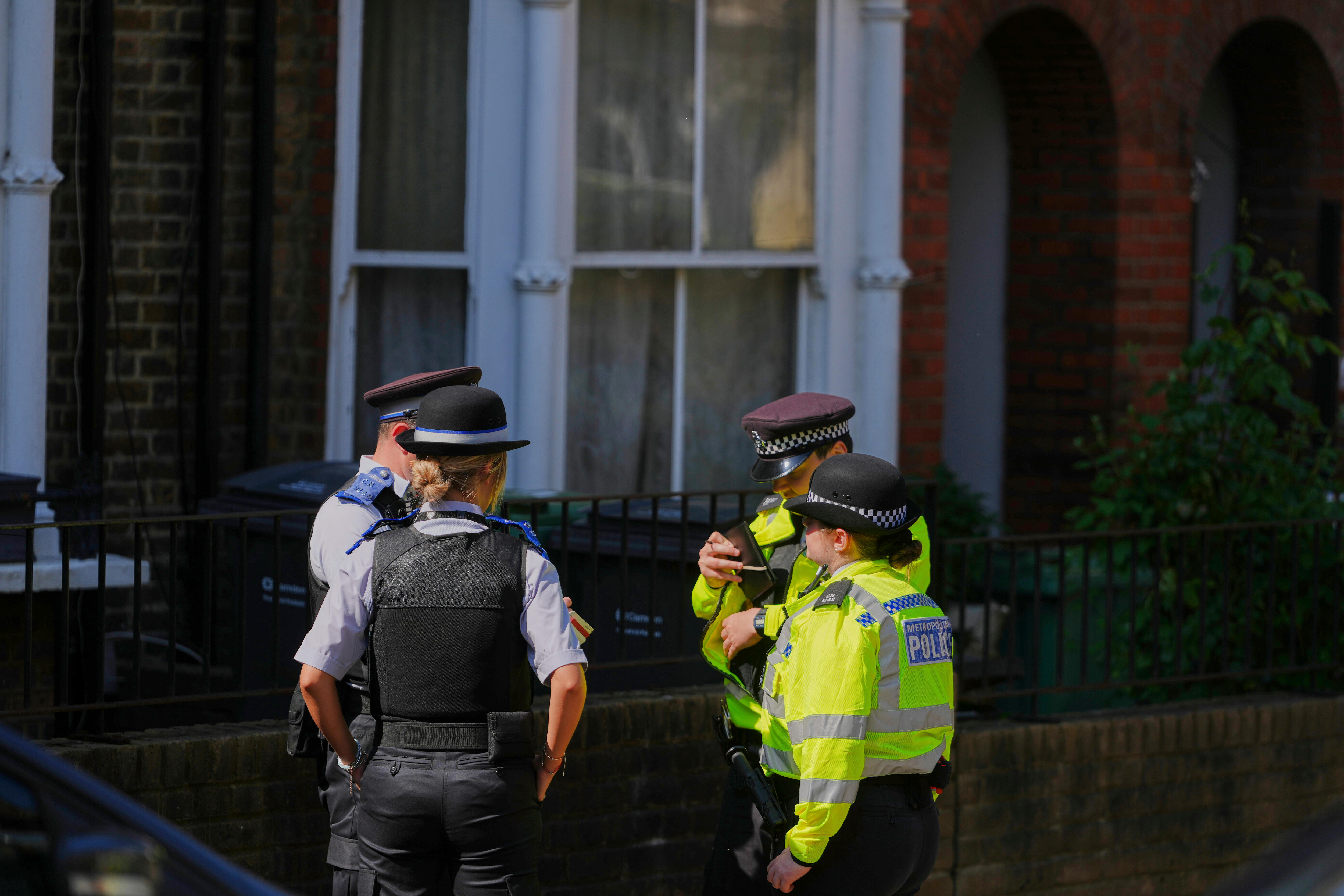 Four police offers talk standing near a house
