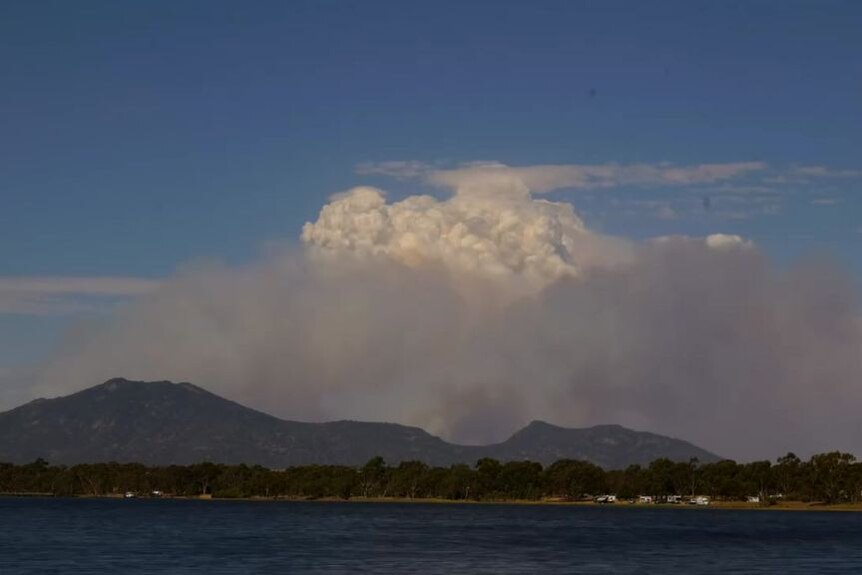 Screengrab of a large plume of smoke over a distant bushfire with a body of water in the foreground