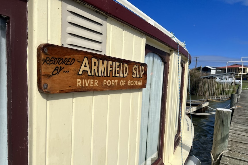 A cream-coloured wooden boat with a sign reading 'Restored by Armfield Slip' on its side