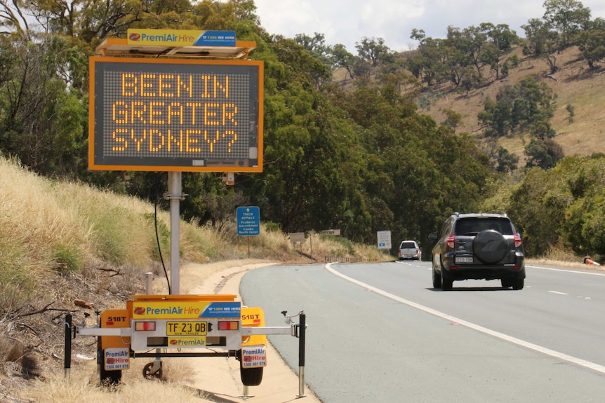 A neon sign on the side of the road asks 'Been in Greater Sydney?" as cars drive towards the capital.