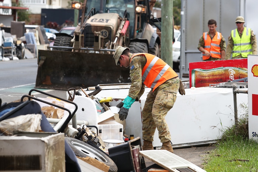 A man in an army uniform piles up rubbish on the street.