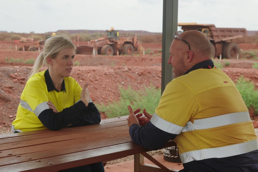 Two people in hi-vis sit chatting at a mine site.