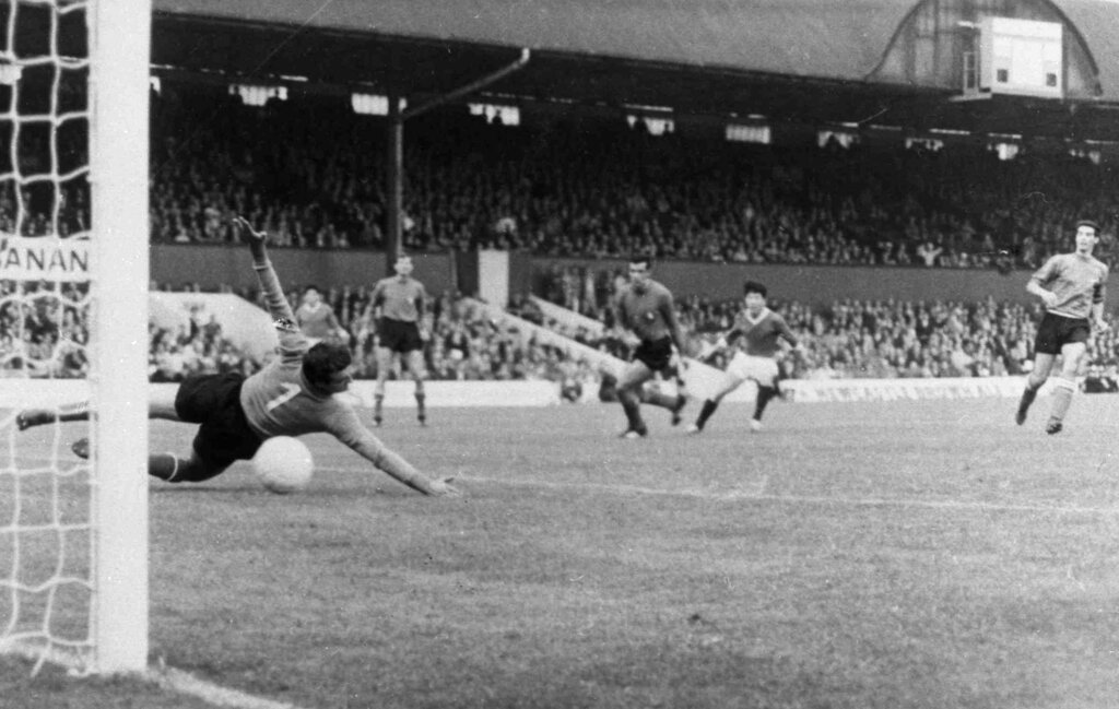 Old image of soccer match taken from behind goal shows Asian player kicking ball past goalkeeper