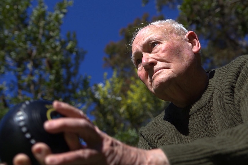 A close up of a man playing lawn bowls prepares to bowl.