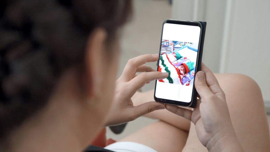 A woman, blurred in the foreground, looks at a shot of her babies on her phone.