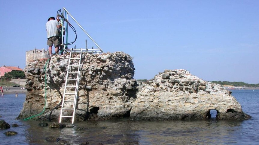 Man stands on top of a concrete wall in the sea collecting samples.