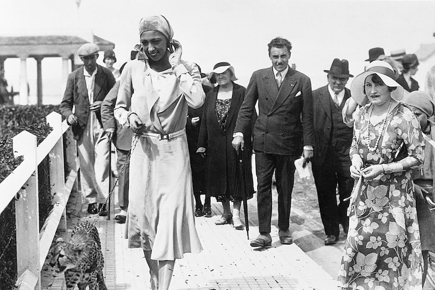 Woman walking on the beach with cheetah surrounded by a crowd 