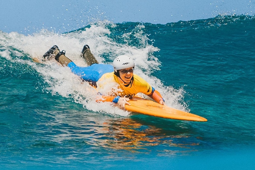 chloe acostada en la tabla de surf bajando frente a la ola cielo soleado 