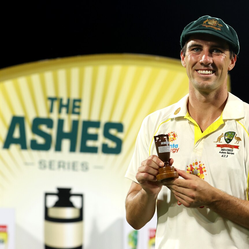 Australian men's cricketer Pat Cummins holds the small Ashes urn in his hands while smiling at the camera