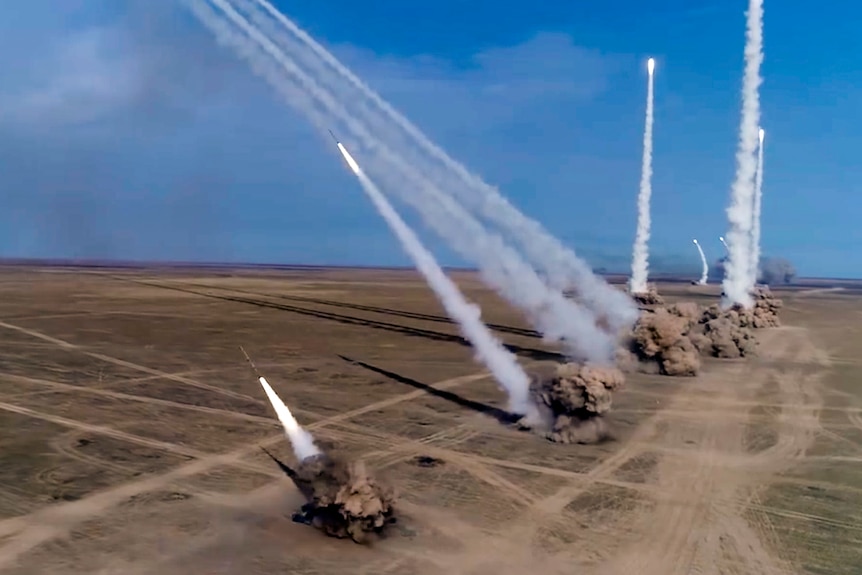 Smoke trails are seen from at least nine rockets launched from vehicles into a blue sky