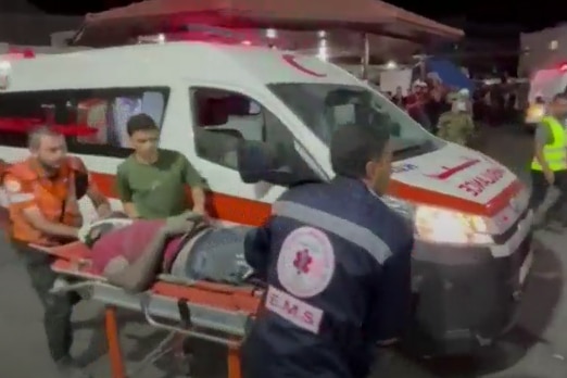 Three people move a stretcher with a man on it who is bandaged up.