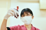 Asian female nurse holding up three vials of blood