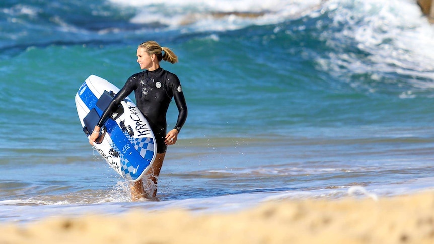 woman in wetsuit in the waves on beach holding a surfboard