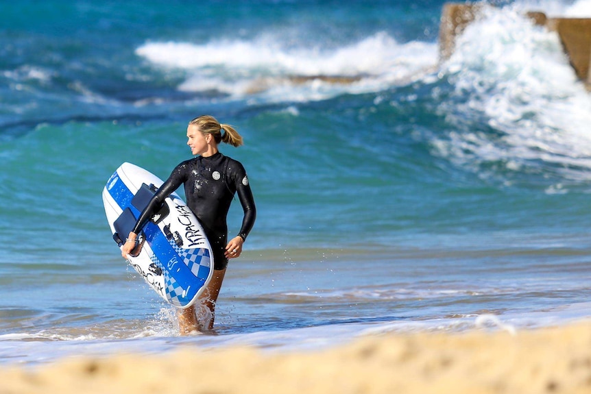 woman in wetsuit in the waves on beach holding a surfboard